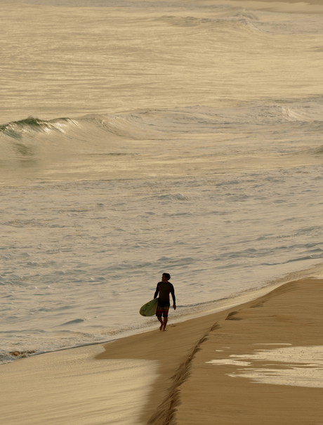 Surfer in wetsuit walking along sandy beach at Amanera.
