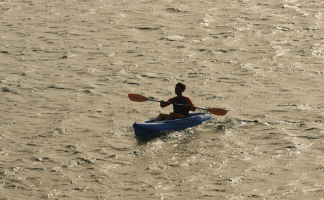 Surfer in dark wetsuit paddling on sandy beach at Amanzoe resort.