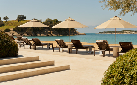 Amanzoe beach club resort dengan sunbeds, payung, dan pemandangan laut Aegean yang tenang.