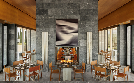 Restaurante principal de Amanzoe con columnas de piedra, mesas de madera y vistas al exterior.