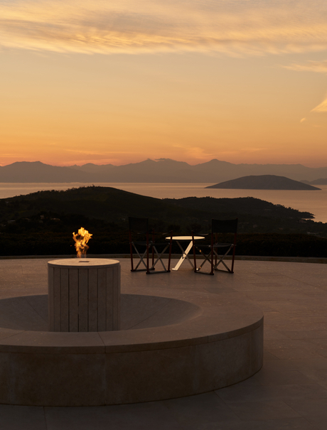 Terrace with dining setup at sunset, Amanzoe resort overlooking distant mountains and sea.