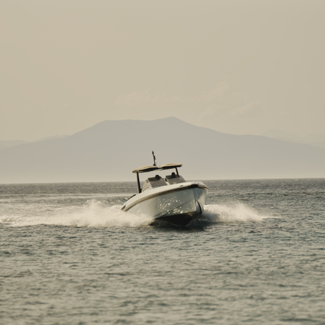 Wally powerboat moored in calm waters at Amanzoe resort, with distant mountains under overcast sky.