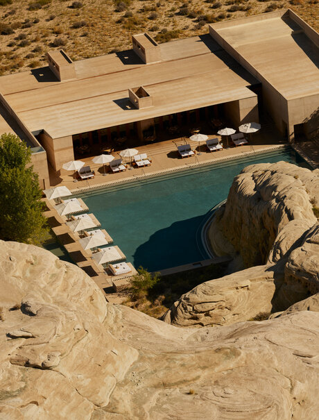 Aerial view of Amangiri's plunge pool carved into desert rock, with resort buildings visible beyond.