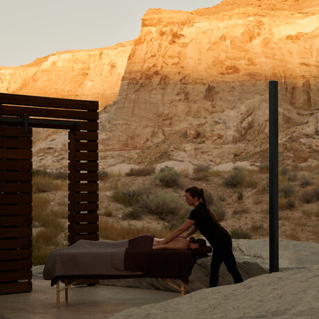 Therapist administering massage treatment at Amangiri wellness spa, with red rock cliffs visible beyond the pavilion.