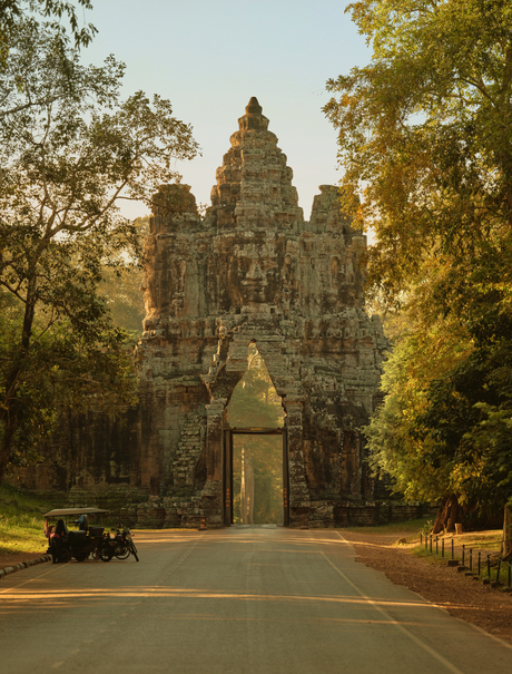 Stone temple tower framed by tree-lined avenue at Amansara, Cambodia, with statue in foreground.