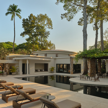 Amansara's main pool pavilion with wooden loungers, surrounded by tropical trees and manicured gardens.