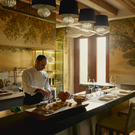 Chef preparing cuisine in Palazzo kitchen at Aman Venice, with golden walls and natural light.