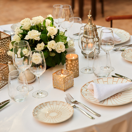 Formal dining table set with cream and gold place settings, white floral centrepiece, and glassware at Amanjena.