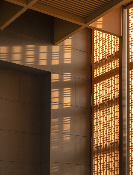Warm light filters through a timber screen at Amanyangyun, casting geometric shadows on a dark wall.
