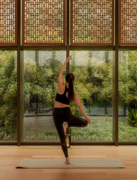Yoga instructor in a standing pose within the Pilates and yoga studio at Amanyangyun, Shanghai, with garden views through large windows.