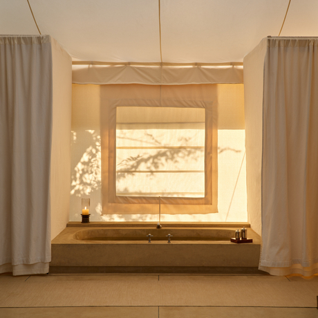 Bathtub set into wooden surround within tent bathroom at Aman-i-Khas, with framed artwork above and sheer curtains either side.