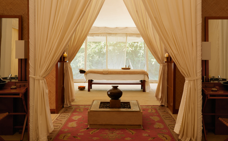 Spa interior at Aman-i-Khas with wooden treatment bed, flowing curtains and views across Indian landscape.