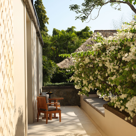 Resort terrace at Aman Villas at Nusa Dua with wooden chair and lush garden views.