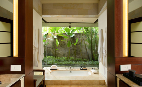 Bedroom at Aman Villas at Nusa Dua with garden view through open doors and tropical plants.