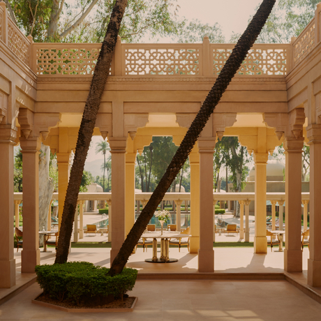 Amanbagh's main restaurant building exterior with geometric latticed windows and a large tree trunk passing through the sandy-coloured colonnade.