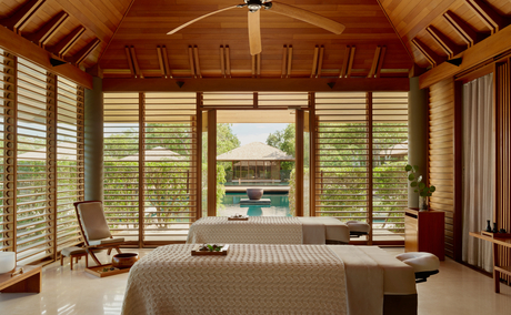 Spa treatment room at Amanyara with wooden ceiling, shuttered windows, and massage table overlooking tropical grounds.