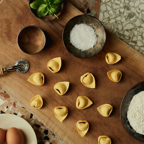 Freshly folded pasta parcels arranged on a wooden surface in the Palazzo kitchen at Aman Venice, surrounded by ingredients including flour and salt.