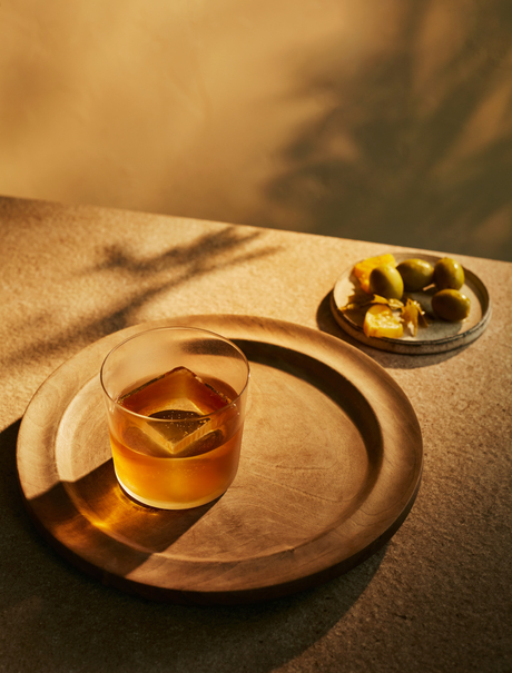 アマンプリのビーチリゾートで、木製のプレートに盛られたウイスキーとシガーが光の中に佇む。