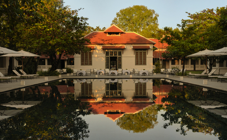 Dining pool at Amantaka with table settings reflected in still water, flanked by lounge chairs and colonial architecture.