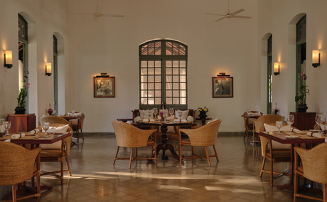 Amantaka's dining room with symmetrical wooden tables, arched window, and soft wall lighting.