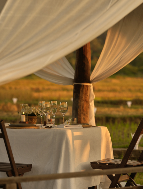 Intimate outdoor dining table set at Amantaka with draped fabric canopy and countryside views at dusk.