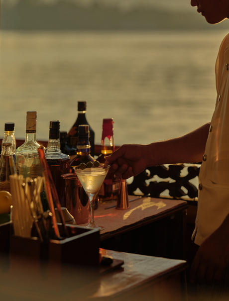 Cocktail-making session during a Mekong sunset cruise at Amantaka, with spirit bottles and mixing tools arranged on a wooden table.