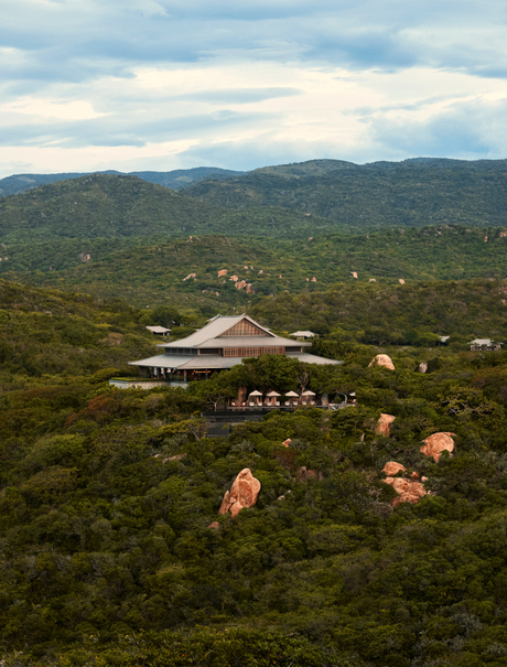 Amanoi's main pavilion nestled within verdant Vietnamese highlands, surrounded by forested mountains under soft clouds.