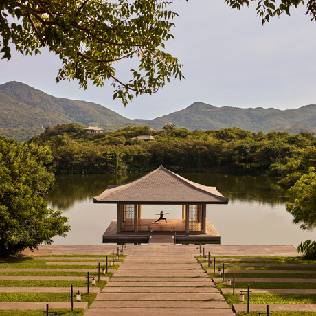 Wooden pavilion with pitched roof extending over still water at Amanoi, surrounded by verdant landscape and distant mountains.