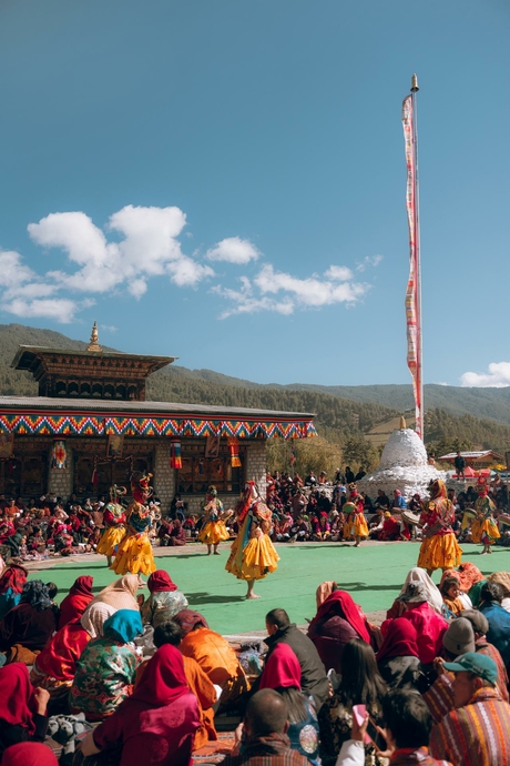 Colourful festival gathering at Amankora in Bumthang, with crowds seated on ground beneath clear blue sky.