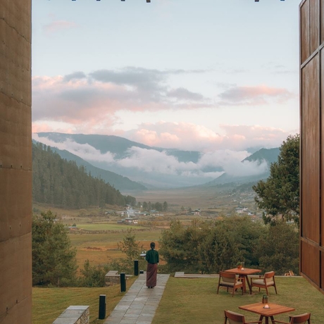 Outdoor dining terrace at Amankora's Gangtey Lodge overlooking a misty valley and forested mountains at dusk.