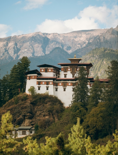 Amankora perched on a cliff in Paro valley, Bhutan, with forested mountains rising behind.
