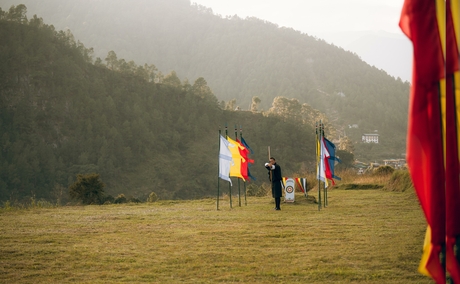 Guests stand in a misty valley meadow at Amankora, with forested mountains rising behind them and a red fabric detail in the foreground.
