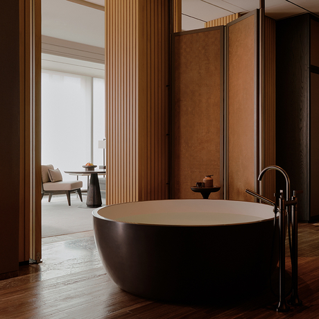 Freestanding black bathtub in a principal bedroom at Aman Nai Lert Bangkok, with wooden panelling and view to adjoining room.
