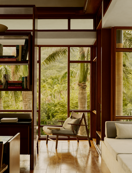Library at Amanera with wooden-framed windows overlooking tropical greenery and a reading chair.