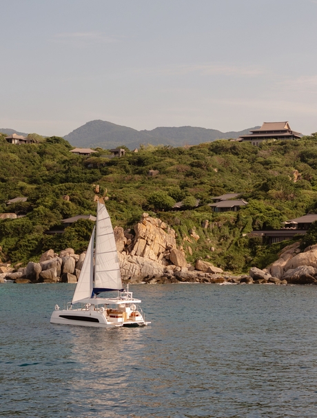 Catamaran sailing on turquoise waters off the Vietnamese coast near Amanoi, with forested hills and mountains in the background.