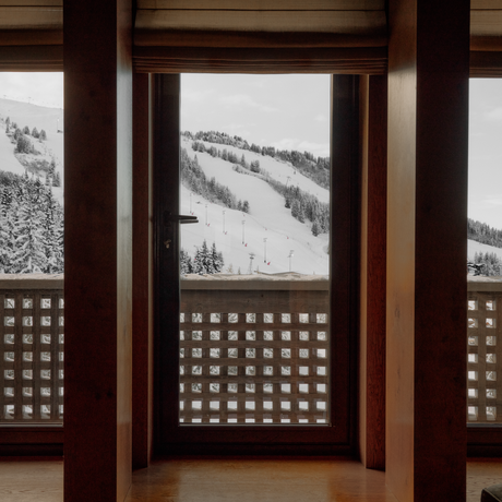 Wooden-framed windows with geometric lattice panels overlooking snow-covered Alpine slopes at Aman Le Mélézin.