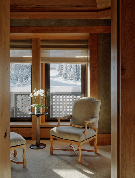 Wooden-framed reading nook at Aman Le Mélézin with upholstered chair overlooking snowy Alpine landscape.