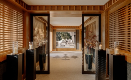 Stone entrance hall at Aman Le Mélézin with wooden walls and open doors framing snowy Alpine views.