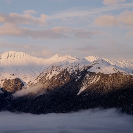 Snow-capped Alpine peaks rise above forested slopes and morning mist at Aman Le Mélézin, France.
