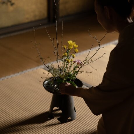 A hand arranging fresh flowers and branches in a dark vessel at Aman Kyoto.