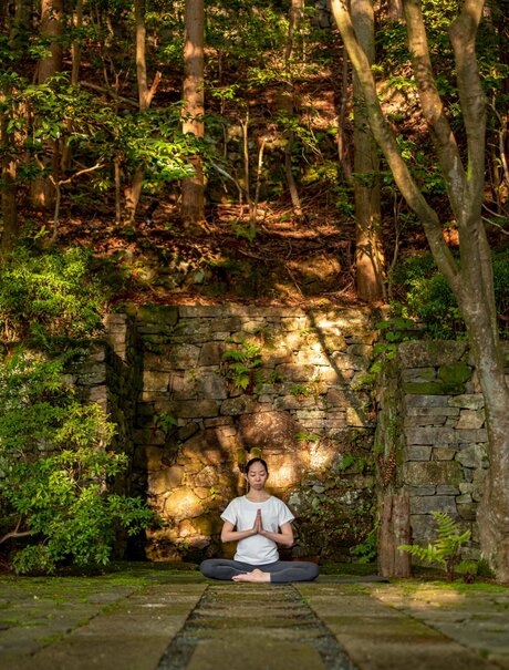 Person practising morning yoga on stone pathway surrounded by moss-covered walls and forest at Aman Kyoto.