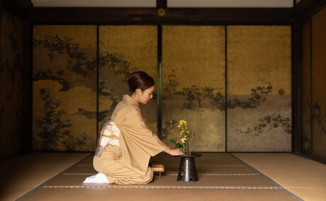 Woman in cream kimono arranging flowers in traditional Japanese room at Aman Kyoto.