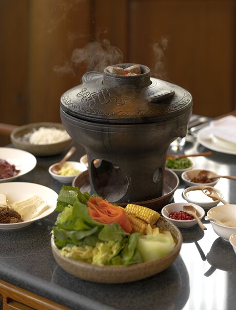 Nixi black pottery hot pot with steam rising, surrounded by small bowls and fresh ingredients at Amandayan.