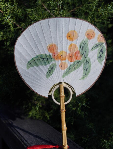 Traditional Chinese fan with painted orange flowers and green leaves, displayed at Amandayan.