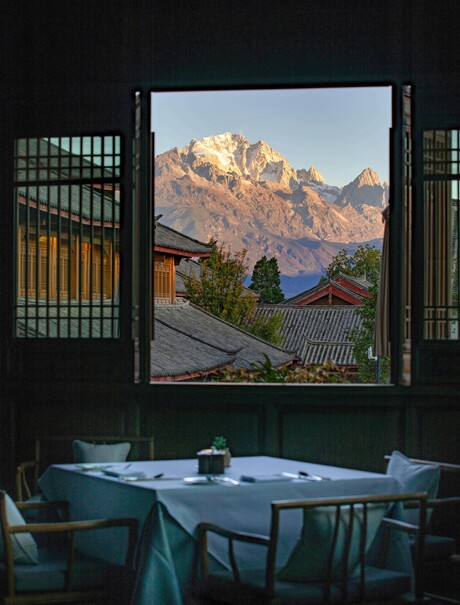 Dining room at Amandayan with mountain views framed by an open window, teal table and chairs in foreground.