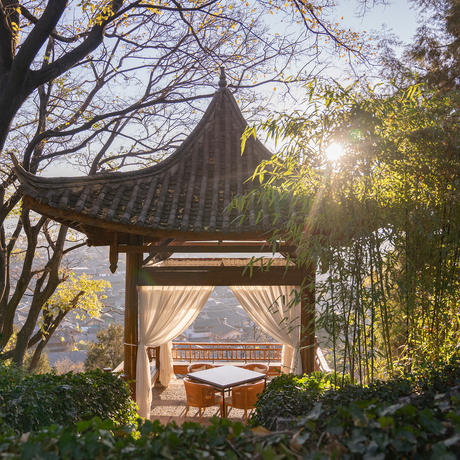 Sunrise light filters through trees beside a traditional pavilion at Amandayan, China resort.