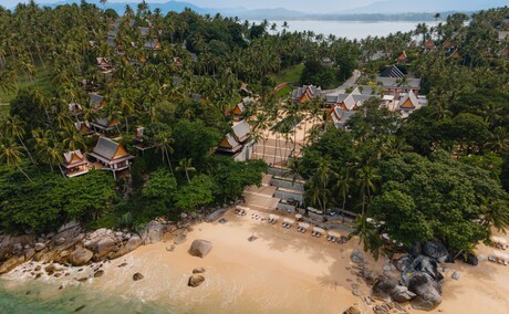 Aerial view of a sandy beach cove surrounded by dense tropical forest at Amanpuri resort, Thailand.