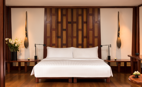 Amanpuri bedroom pavilion with wooden feature wall, pendant lights and white bed.