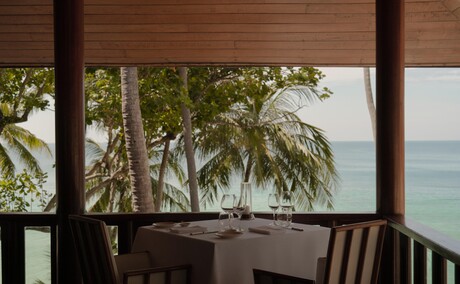 Table setting in Arva dining venue at Amanpuri resort, Thailand, with ocean views and palm trees.