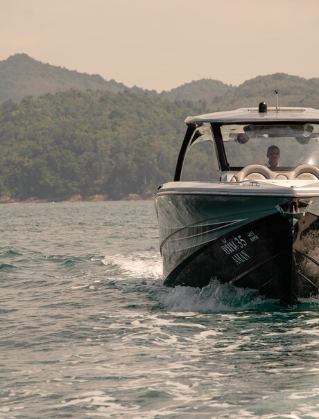 Speedboat moored in turquoise waters with forested island backdrop at Amanpuri resort, Thailand.